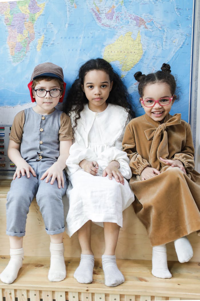 services-img Three children in playful outfits sitting indoors against a world map backdrop.